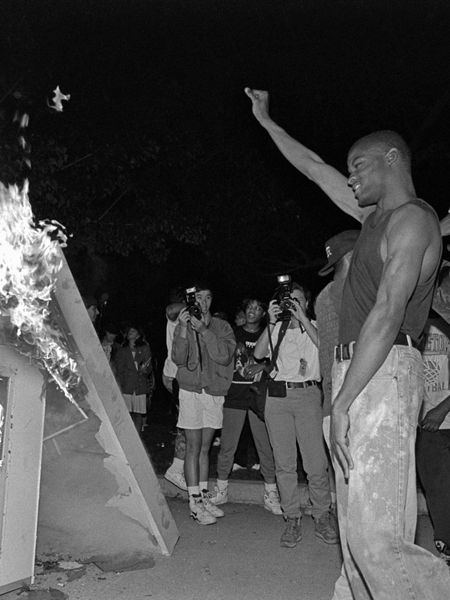 Ein Mann reckt seine Faust in die Höhe, vor ihm brennt ein Kiosk