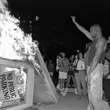Ein Mann reckt seine Faust in die Höhe, vor ihm brennt ein Kiosk