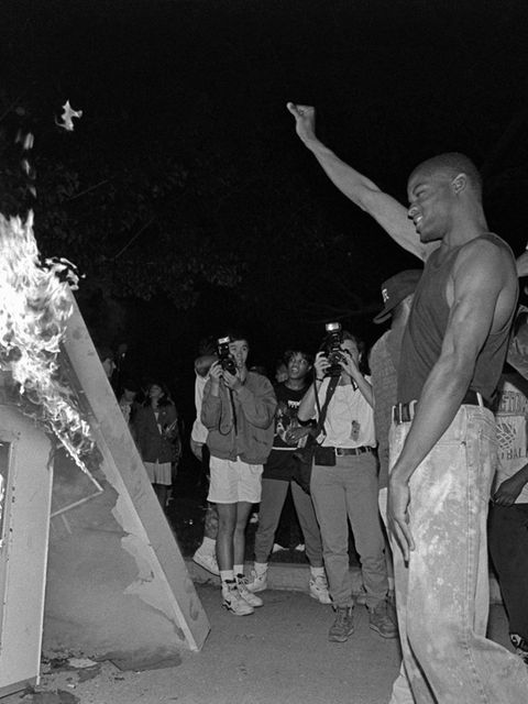 Ein Mann reckt seine Faust in die Höhe, vor ihm brennt ein Kiosk