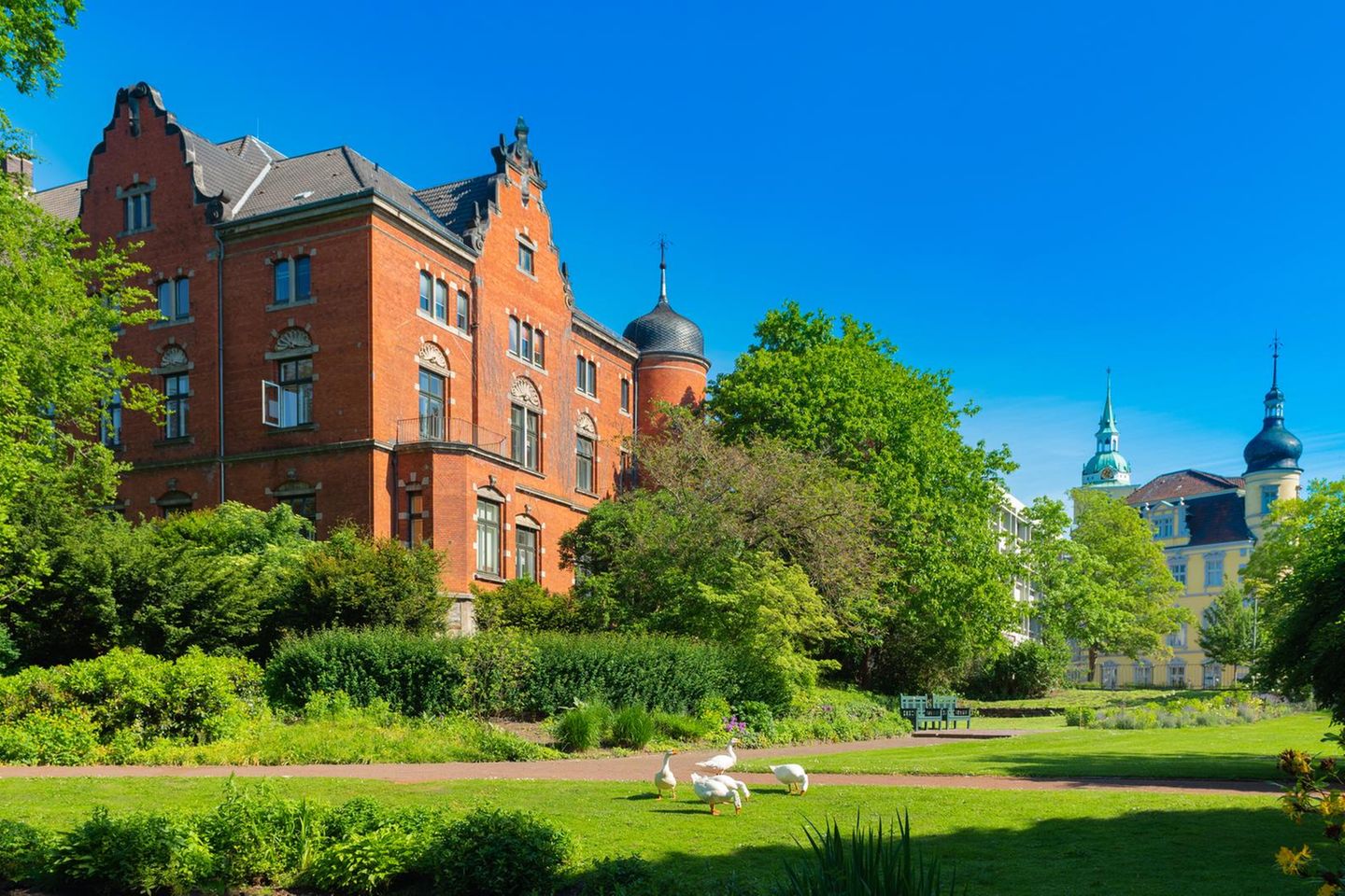 Rote Backsteinfassade, umgeben von üppigem Grün: Das Elisabeth-Anna-Palais blickt auf den Schlossteich mit seinen Gänsen. Es liegt am Rand des weitläufigen Schlossgartens im Herzen Oldenburgs. Zusammen mit den Wallanlagen und dem Botanischen Garten zählt der historische Park zu den schönsten Grünflächen der Stadt. Baumriesen, Blumenbeete, verschlungene Wege und Bachläufe laden hier zum Verweilen ein.