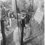 Ein Bauarbeiter sitzt auf einem Stahlträger in mehreren Metern Höhe über der Skyline von New York