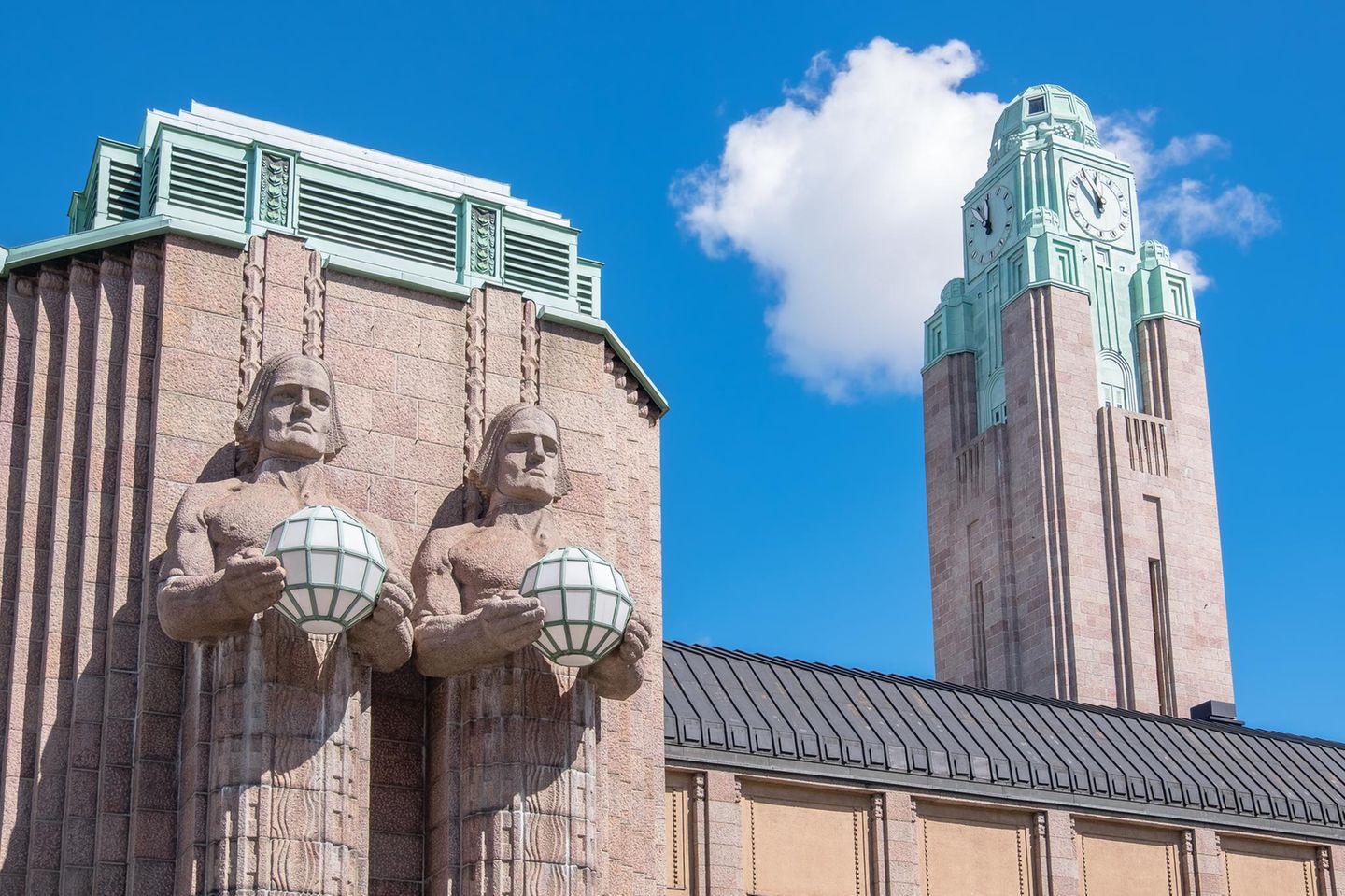 Turm und Statuen am Hauptbahnhof Helsinki, im Hintergrund blauer Himmel mit Wolke