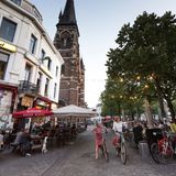 Café-Gäste und zwei Radfahrerinnen im Viertel Zurenborg vor Kirchturm