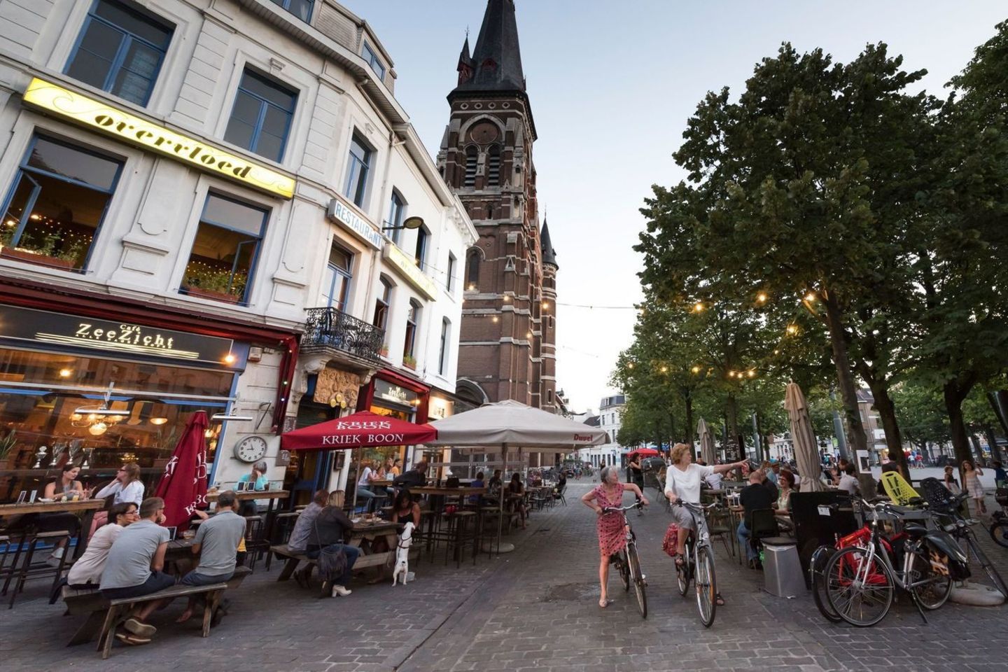Café-Gäste und zwei Radfahrerinnen im Viertel Zurenborg vor Kirchturm