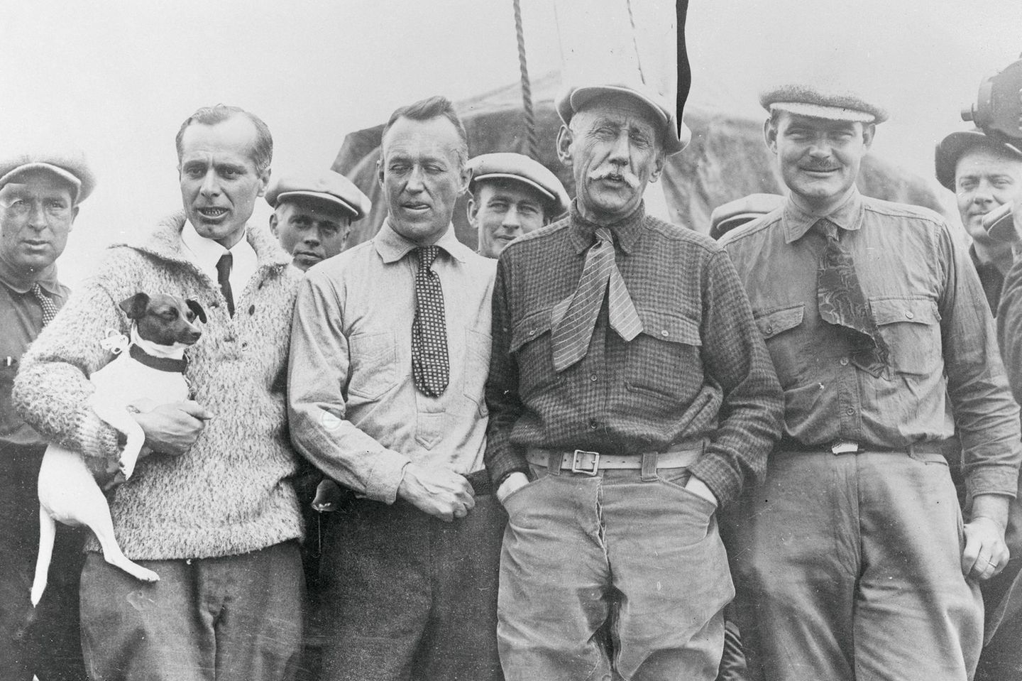 Nobile, der seinen Hund auf dem Arm hält, steht neben Ellsworth und Amundsen sowie weiteren Männern der Crew.
