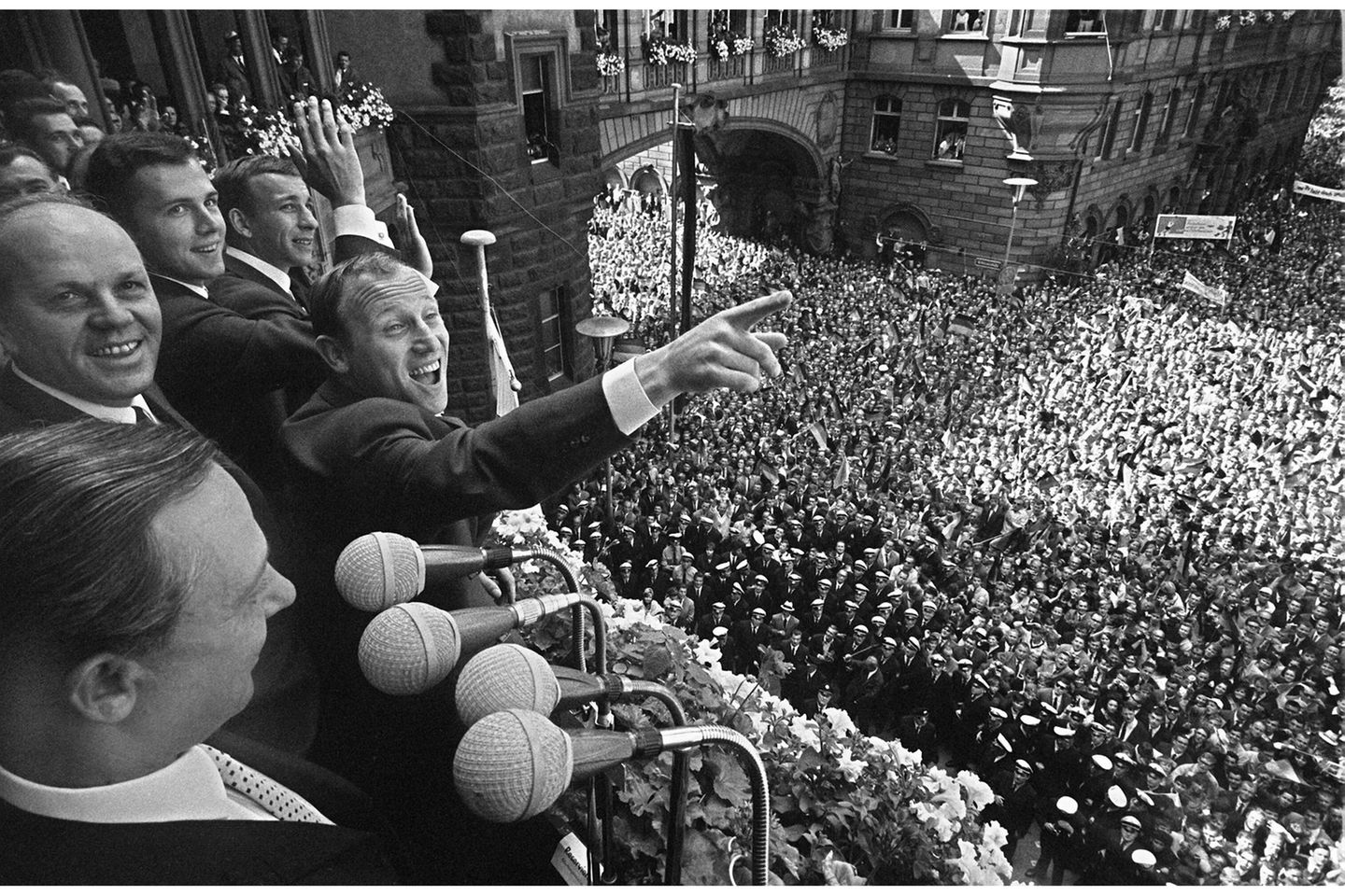 Eine begeisterte Menge füllt am 31. Juli 1966 den Frankfurter Römerberg und jubelt der deutschen Nationalmannschaft auf dem Balkon des Rathauses zu. Vorn steht Oberbürgermeister Willi Brundert, in der Mitte Uwe Seeler mit ausgestrecktem Zeigefinger, dahinter der junge Franz Beckenbauer. Erst einen Tag zuvor hatte England das WM‑Finale in Wembley nach Verlängerung mit 4:2 gewonnen – doch trotz der Niederlage feiern die Fans "ihre" Vizeweltmeister wie Sieger.