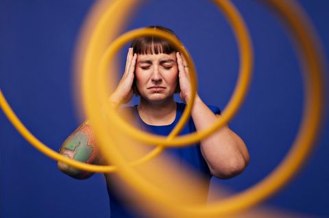 vestibuläre Migräne: Eine Frau hält sich den Kopf, umgeben von Spiralen
