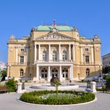 Nationaltheater mit Säulen und Fahne, davor angelegter Garten mit Bänken