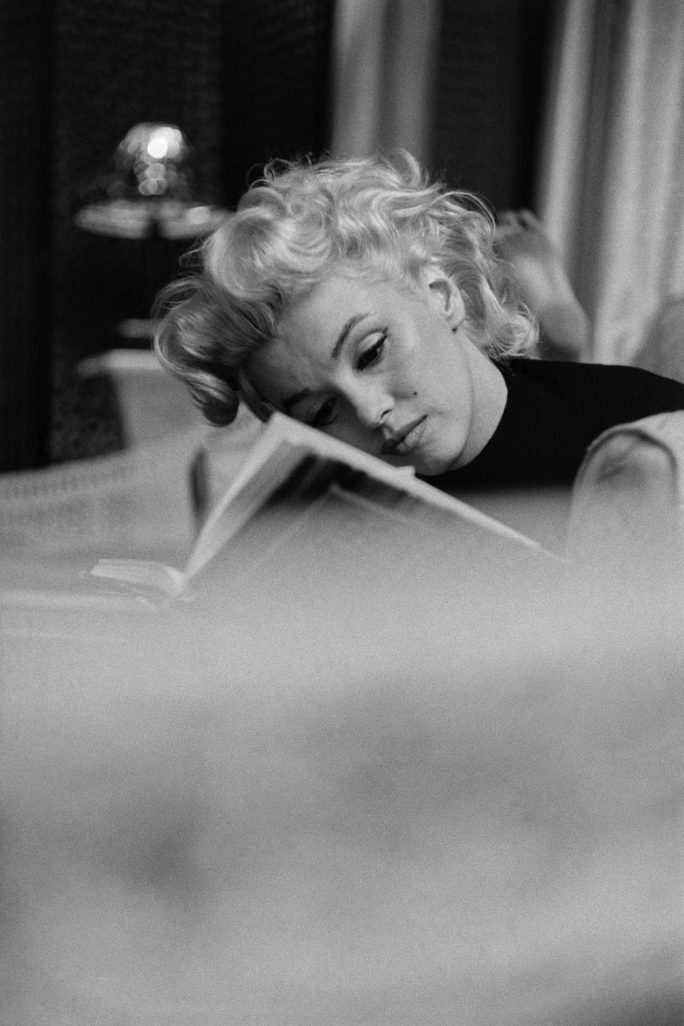 Marilyn Monroe liest konzentriert in einem Buch im Sessel sitzend im Jahr 1955