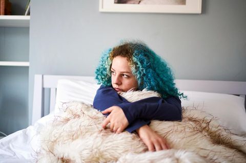 Junge Frau sitzt allein auf einem Bett und schaut aus dem Fenster