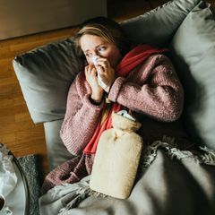 Eine erkältete Person liegt auf einem Sofa